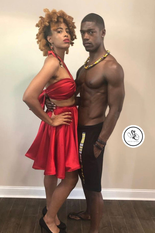 Sheridonna Designs custom streetwear for him and her. The women is wearing a matching rich red satin halter like top design with bow in back and a knee length circle shirt . The men is wearing a black fitted knee length custom blend shorts; with one horizontal line in the front from waist to hem i